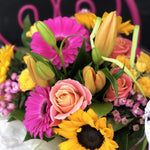 A beautifully colourful bouquet of fuschia pink gerberas, apricot lilies, sunflowers, peachy-pink roses and bouvardia, hand-tied, aqua-packed and presented in a gift bag with tissue paper.