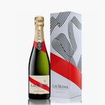 Green bottle with a label for G H mumm Champagne and a gold foil seal is stood next to a gift box 