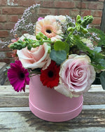 Pink and cream flowers that include roses in what could be a pink hat box that would be an ideal gift for Mother's Day