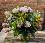 Bouquet of flowers that are cream roses and pink tulips in front of a brick wall 