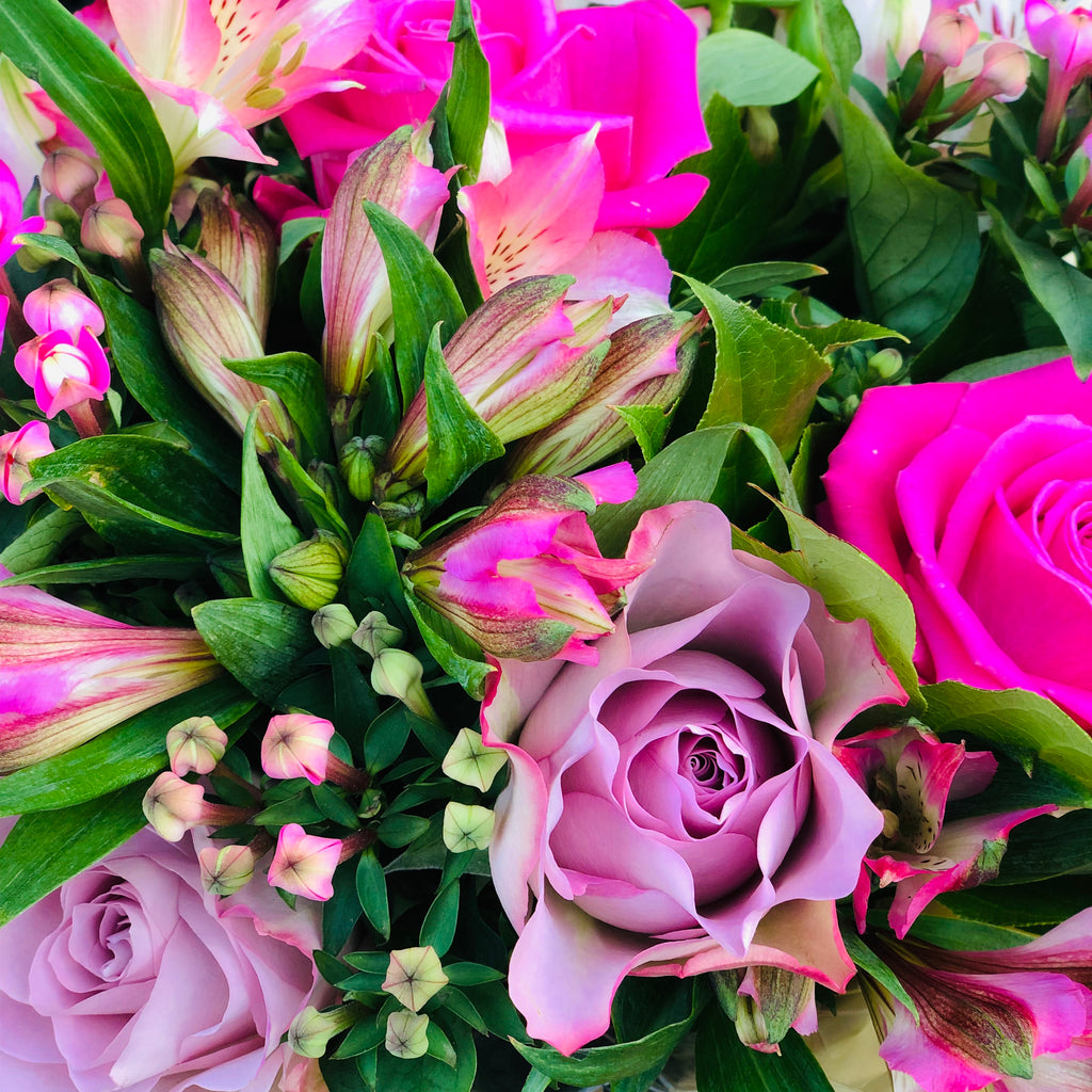 A hand-tied bouquet of dusky and rich pink roses, pink bouvardia and alstromeria flowers,  which is presented in an aqua-packed gift bag with tissue paper.