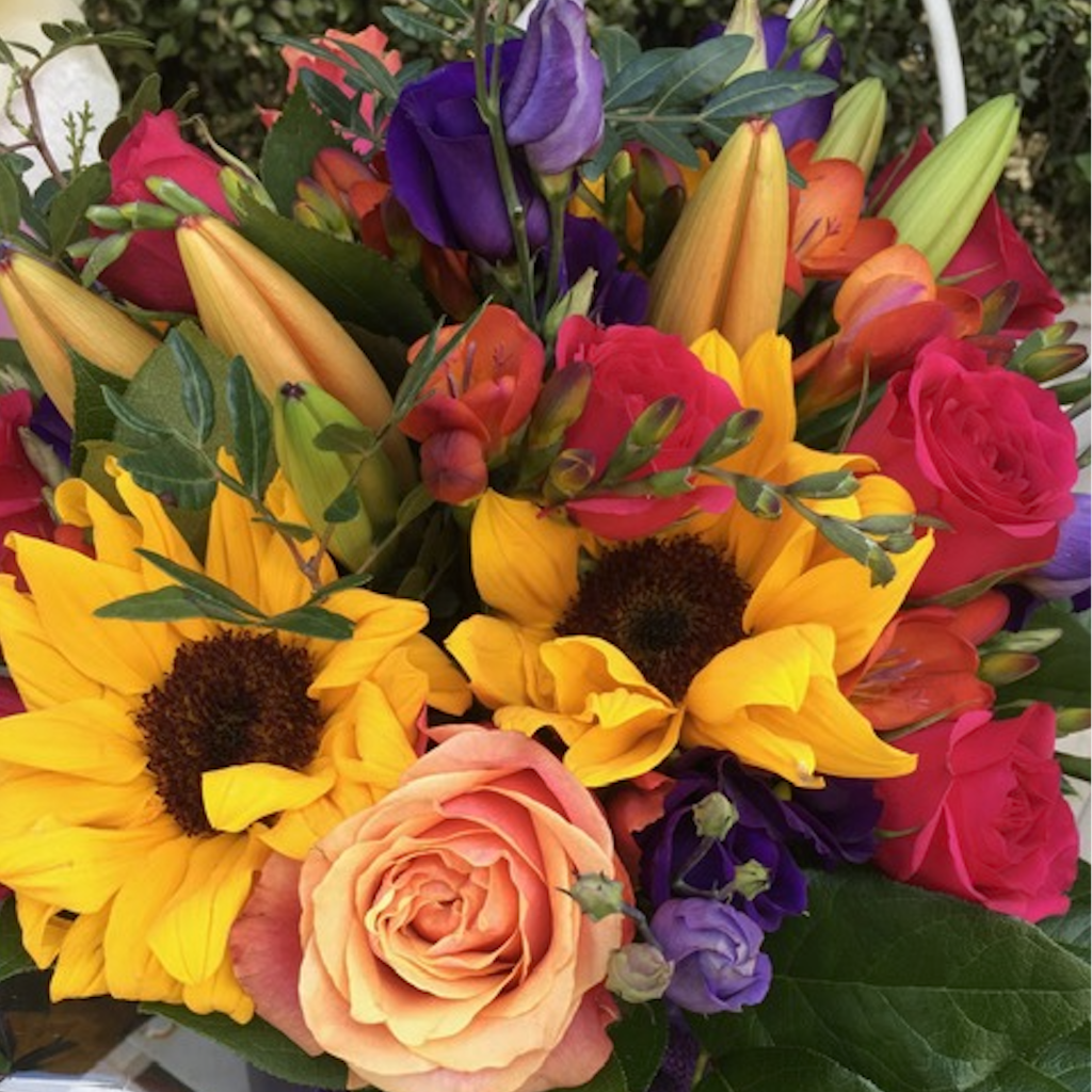 A stunning and bright bouquet including Sunflowers, Roses, Tulips, Lisianthus, Freesias and Lillies. Hand-tied in an aqua-pack and presented in a gift bag.