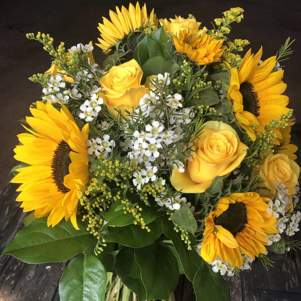 A bright bouquet of sunflowers, yellow roses, wax flower, and Solidago.  Aqua-packed and presented in a gift bag.