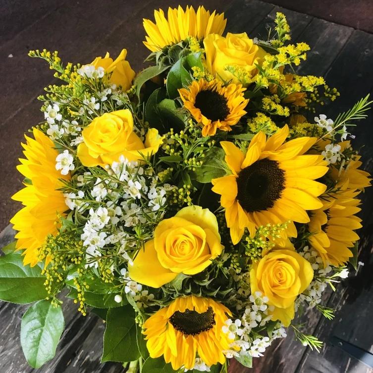 A bright bouquet of sunflowers, yellow roses, wax flower, and Solidago.  Aqua-packed and presented in a gift bag.